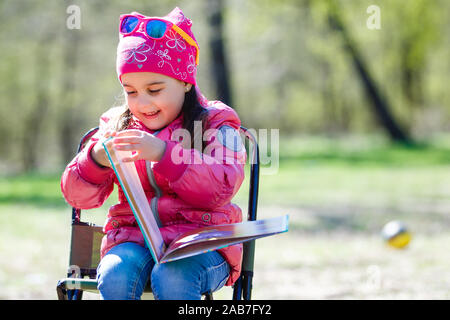 Kleines Mädchen sitzen in übergroßen Schaukelstuhl vorgibt, ihre Teddybären zu lesen. Stockfoto