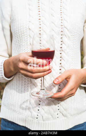 Ein Mädchen in einem weißen Herbst Pullover hält ein Glas Wein in der Hand. Weinlese Konzept. Stockfoto