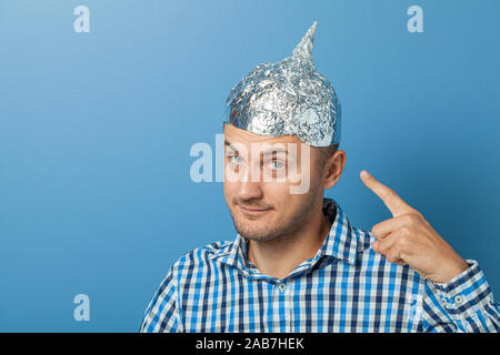 Mann mit Lächeln und zeigt mit dem Finger auf einen Hut mit Aluminiumfolie. Schützt vor lesen Denken. Stockfoto