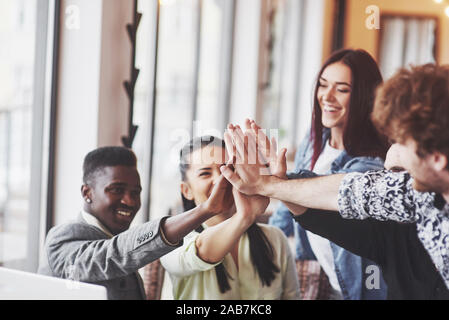 Glückliche junge Unternehmer in Freizeitkleidung am Café-Tisch oder Geschäftsstelle gibt hohe Fives miteinander, als ob Erfolg feiern oder starten Stockfoto