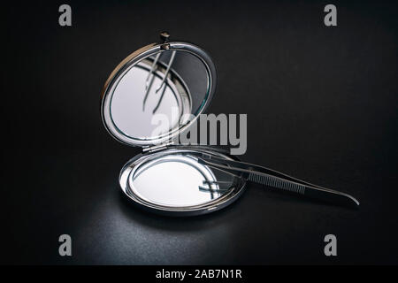 Faltbare Pocket Mirror und Pinzette auf eine dunkle Oberfläche Stockfoto
