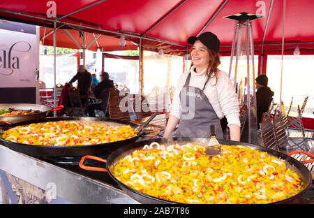 Eine lächelnde Frau verkaufen Paella aus riesigen Pfannen auf dem Fischmarkt in Bryggen, Bergen, Norwegen, Skandinavien, Europa Stockfoto