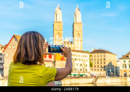 Ansicht der Rückseite Frau fotografieren Grossmünster Cathedral und Limmat mit Smartphone, Zürich, Schweiz, Europa Stockfoto