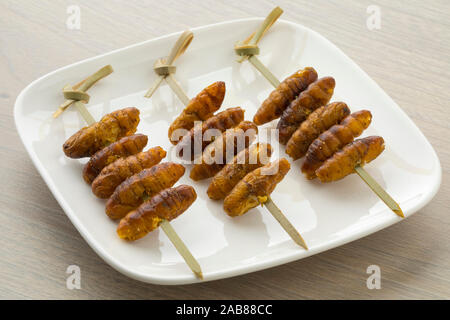 Teller mit knusprigen Seidenraupen auf einem Stick für einen Snack Stockfoto