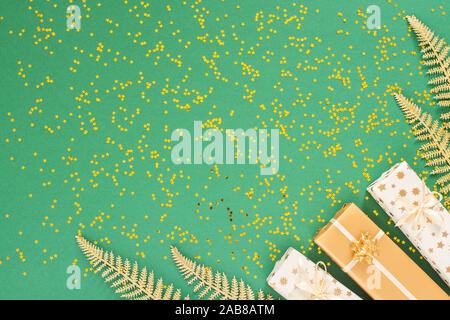 Helle glänzende goldene Farnblätter und Geschenkboxen auf grünem Hintergrund mit Glitter gold Sterne, Flach, Ansicht von oben, kopieren Raum Stockfoto
