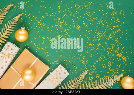 Helle glänzende goldene Farnblätter und Geschenkboxen mit Weihnachten Kugeln auf einem grünen Hintergrund mit Glitter gold Sterne, Flach, Ansicht von oben, kopieren Raum Stockfoto