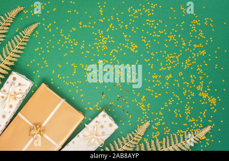 Helle glänzende goldene Farnblätter und Geschenkboxen auf grünem Hintergrund mit Glitter gold Sterne, Flach, Ansicht von oben, kopieren Raum Stockfoto