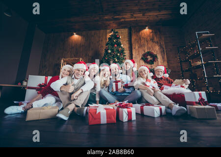 Foto fröhliche, positive große Familie umgeben mit Gift boxed lächelnd toothily vor weihnachtsbaumbeleuchtungen Kranz in santa hut Cap angezeigt Stockfoto