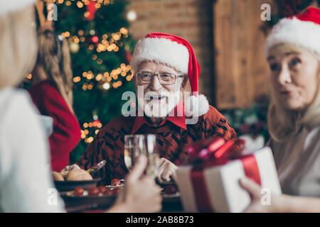 Phot von Großvater positive fröhlich lächelnd in Brillen Brillen Tragen santa hut Kopfbedeckung Gefühl festliche Stimmung im Gespräch mit Gästen Stockfoto