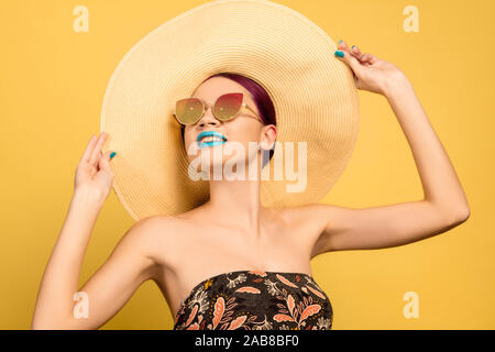 Porträt der schönen Frau mit hellen Make-up, Hut und Sonnenbrille auf Gelb studio Hintergrund. Elegantes und Modisches und Frisur. Die Farben des Sommers. Beauty, Fashion und Ad-Konzept. Stockfoto