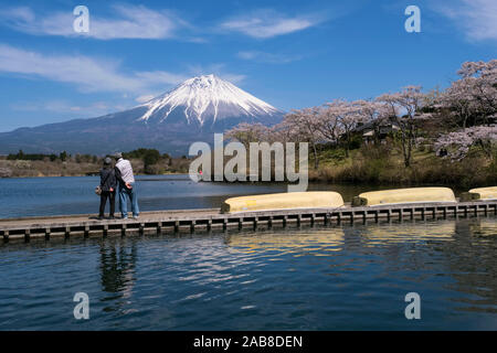 Japan, Fujinomiya, Präfektur Shizuoka: Mount Fuji mit seiner schneebedeckten Gipfel vom See Tanuki gesehen. Paar japanischen Touristen auf einem Ponton suchen Stockfoto