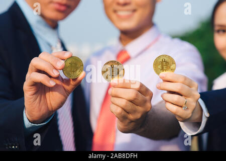 Junge asiatische Geschäftsmann und Goldene bitcoin vor seinem Internationalen multi-ethnische Teams in der modernen Stadt. Stockfoto