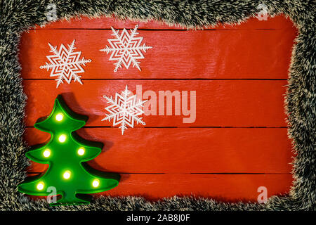 Weihnachten Zusammensetzung auf rote Holzbrett mit Christmas Garland und Dekorationen. Kreative Zusammensetzung mit Rand kopieren und Raum, Ansicht von oben, flach. Stockfoto
