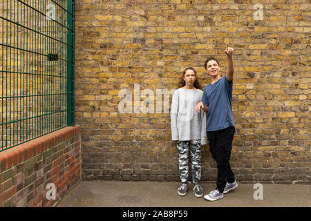 Ein paar, Junge und Mädchen, stehen vor einer Mauer und schauen Sie in den Himmel, an ihn gerichtet. Stockfoto