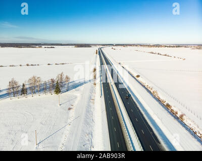 Schöne Luftaufnahme von Schnee bedeckten Felder mit einer zweispurigen Straße zwischen Bäumen. Rime Eis und Raureif auf den Bäumen. Malerische Winterlandschaft in der Nähe von Vi Stockfoto