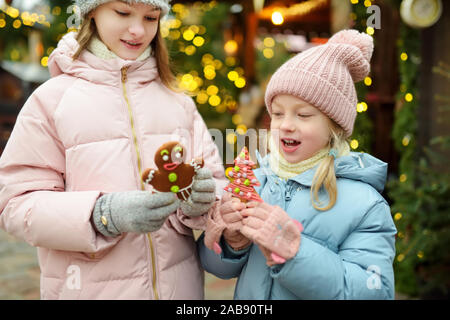 Zwei adorable Schwestern in Lebkuchen Cookies auf den traditionellen Weihnachtsmarkt in Riga, Lettland. Kinder mit Süßigkeiten, Bonbons und Lutscher auf Weihnachten Stockfoto