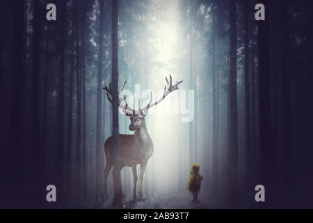 Ein kleines Kind steht vor einem großen Hirsch im dunklen Nebelwald Stockfoto