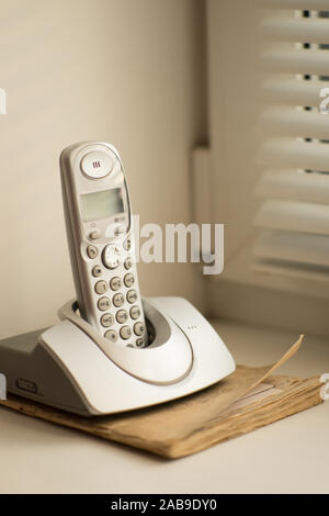 Telefon steht auf dem alten Telefonbuch auf der Fensterbank mit Fensterläden. Stockfoto