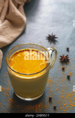 Traditionelle indische Gelbwurz latte Trinken mit Gewürzen auf dunkelblauem Hintergrund mit gewürzen bestreut. Vertikale Foto, Platz für Text. Stockfoto