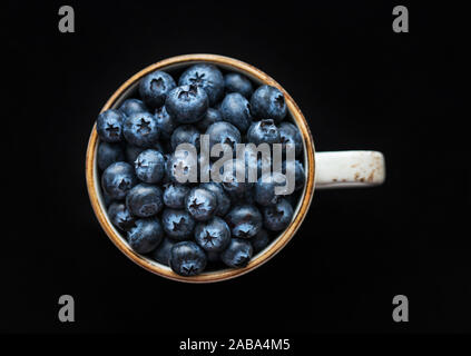 Frische Heidelbeeren in einer Tasse auf einem schwarzen Hintergrund. Ansicht von oben, Makro. Blaue reife Beeren Nahaufnahme. Essen Hintergrund. Stockfoto