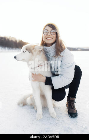 Glückliche junge Mädchen spielen mit sibirischen Husky Hund in Winter Park. Sie gehen auf einem zugefrorenen See Stockfoto