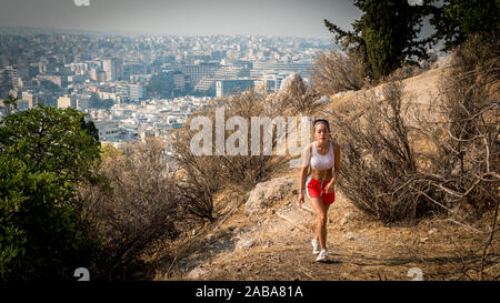 In roten Hosen und weißen Turnschuhen auf Trail auf den Berg mit der Stadt Athen im Hintergrund jugendlich Stockfoto