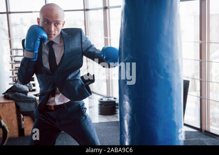 Eine verärgerte kahlen Geschäftsmann schlägt ein Boxing Birne in der Turnhalle. Konzept der Anger Management Stockfoto