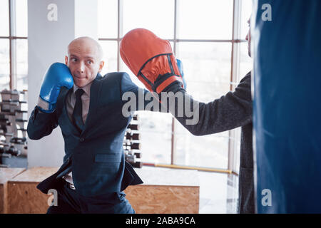 Eine verärgerte kahlen Geschäftsmann schlägt ein Boxing Birne in der Turnhalle. Konzept der Anger Management Stockfoto