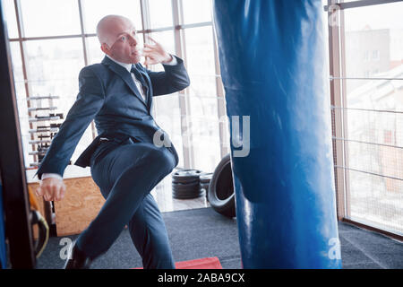 Eine verärgerte kahlen Geschäftsmann schlägt ein Boxing Birne in der Turnhalle. Konzept der Anger Management Stockfoto