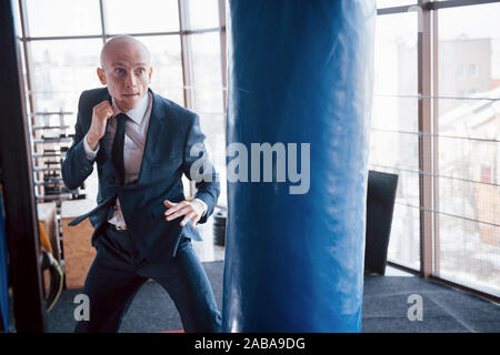 Eine verärgerte kahlen Geschäftsmann schlägt ein Boxing Birne in der Turnhalle. Konzept der Anger Management Stockfoto