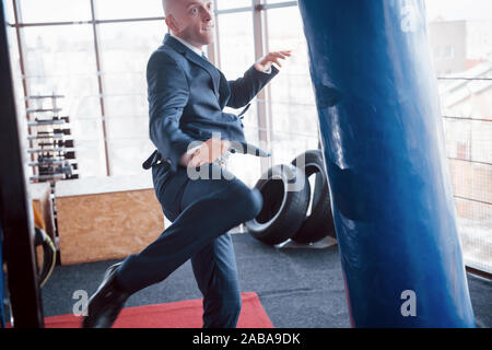 Eine verärgerte kahlen Geschäftsmann schlägt ein Boxing Birne in der Turnhalle. Konzept der Anger Management Stockfoto