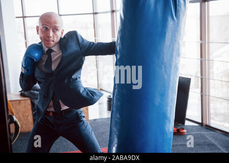 Eine verärgerte kahlen Geschäftsmann schlägt ein Boxing Birne in der Turnhalle. Konzept der Anger Management Stockfoto