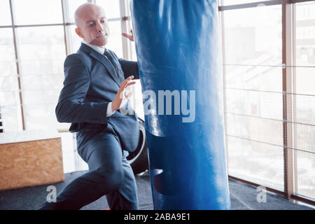 Eine verärgerte kahlen Geschäftsmann schlägt ein Boxing Birne in der Turnhalle. Konzept der Anger Management Stockfoto