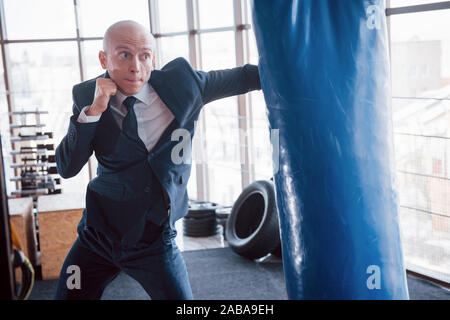 Eine verärgerte kahlen Geschäftsmann schlägt ein Boxing Birne in der Turnhalle. Konzept der Anger Management Stockfoto