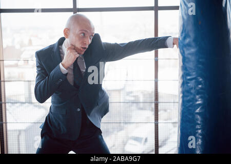 Eine verärgerte kahlen Geschäftsmann schlägt ein Boxing Birne in der Turnhalle. Konzept der Anger Management Stockfoto