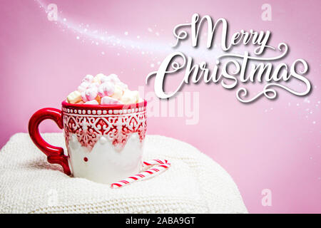 Red christmas Mug mit Marshmallows, Zuckerrohr auf einer gemütlichen Pullover und rosa Hintergrund mit dem Zitat Frohe Weihnachten Stockfoto