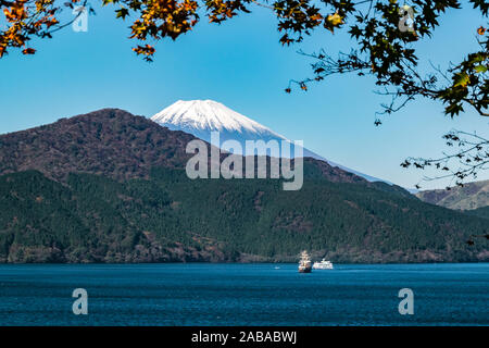 Mt. Fuji von See Ashinoko mit zwei touristische Cruise Boote gesehen, Schuß durch Herbst Laub. Stockfoto