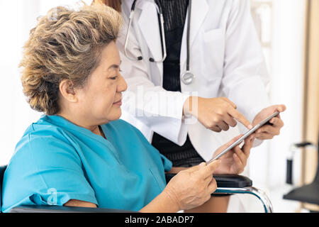 Asiatische vertrauen Arzt mit digitalen tablet Ausdruck Gesundheit Interessen mit alten ältere Frau Patienten sitzen auf Rollstuhl Stockfoto