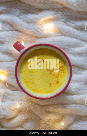 Hot warme Winter trinken Gelbwurz golden Milch auf gemütlichen beige gestrickter Hintergrund mit Lichterketten Stockfoto