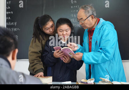 (191119) - NANCHANG, November 26, 2019 (Xinhua) - Er erklärt Xingwu in Gebärdensprache zu zwei Studenten in Sanlian Sonderschule in Nanchang, der ostchinesischen Provinz Jiangxi, Nov. 22, 2019. Er Xingwu, hörgeschädigt, ist ein Lehrer in Sanlian Sonderschule gegründet im Jahr 1994. Fünf Jahre später, die Gründer verstorben. Aus Gründen der Anhörung - der sehbehinderten Kindern den Zugang zu Bildung, Er bestimmt alle Verantwortlichkeiten innerhalb der Schule zu übernehmen. Seine Frau, die er Runmei, auch Hörgeschädigte, widmete sich die Schule und begann Pflege des täglichen Lebens der Kinder zu nehmen. Konsi Stockfoto