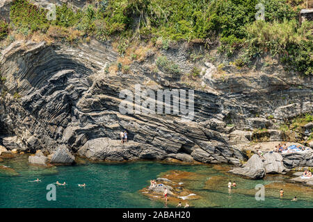 Cliff und Mittelmeer, Vernazza Dorf. Menschen schwimmen oder ein Sonnenbad nehmen. Cinque Terre, UNESCO-Weltkulturerbe. Vernazza, La Spezia, Ligurien, Italien Stockfoto