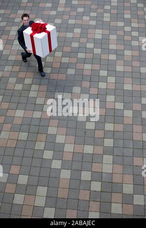 Man überquert einen Innenhof mit einem großen Geschenk mit roter Schleife verpackt Stockfoto