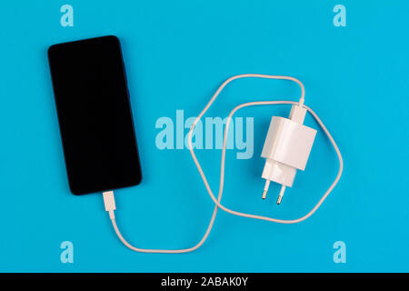 Smartphone mit schwarzen Bildschirm und weißen Lade kabel auf blauem Hintergrund Top View close up Stockfoto