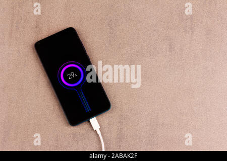 Smartphone mit Batterieanzeige auf dem Bildschirm mit weißen Lade kabel auf rosa-grauen Hintergrund mit Kopie Raum Top View close up Stockfoto