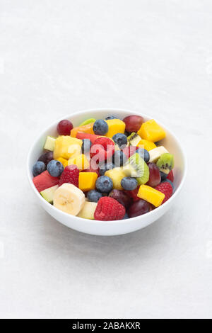Schüssel, auf dem geschnittenes Obst auf einem weißen Hintergrund. Obst Himbeeren, Heidelbeeren, Bananen, Trauben, Mango, Ananas, Melone, Kiwi, Birne Stockfoto
