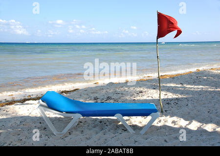 Eine rote Warnfahne und ein Strandstuhl an einem Strand Stockfoto