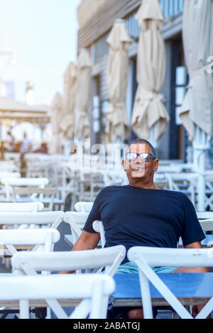 Sportliche Aktivität älterer Menschen glücklich lächelnde Mann im Restaurant sitzen. Senior cafe Eigentümer an einem Tisch sitzen und an der Kamera glücklich. Stockfoto