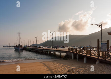 Ilha Grande, Brasilien. 24. Dezember, 2012. Im sonnigen Morgen Blick auf Segelschiff schoner Agua Viva III bei Cais Turistico da Vila günstig Sie Santorini (touristische Pier von Santorini Dorf) und Estacao Santorini Santorini (Ferry Terminal) am Sandstrand mit Sonnenstrahlen, die durch die Berge bei Vila do Santorini Santorini (Dorf), die Ilha Grande (Grosse Insel), die Gemeinde von Angra dos Reis, Bundesstaat Rio de Janeiro, Brasilien. Am 5. Juli 2019, Ilha Grande wurde von der UNESCO als Weltkulturerbe eingetragen. Stockfoto