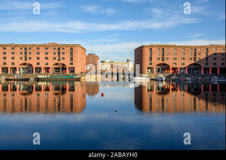 Blick über das Albert Dock in Liverpool zu einer Brücke. Die Gebäude, die Brücke und die Boote sind in der blusr Wasser an einem sonnigen Tag wider. Stockfoto