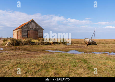 Thornham, Norfolk, England, Großbritannien - 24 April 2019: Eine alte Scheune im Thornham alter Hafen mit einem hölzernen Segelboot daneben Stockfoto